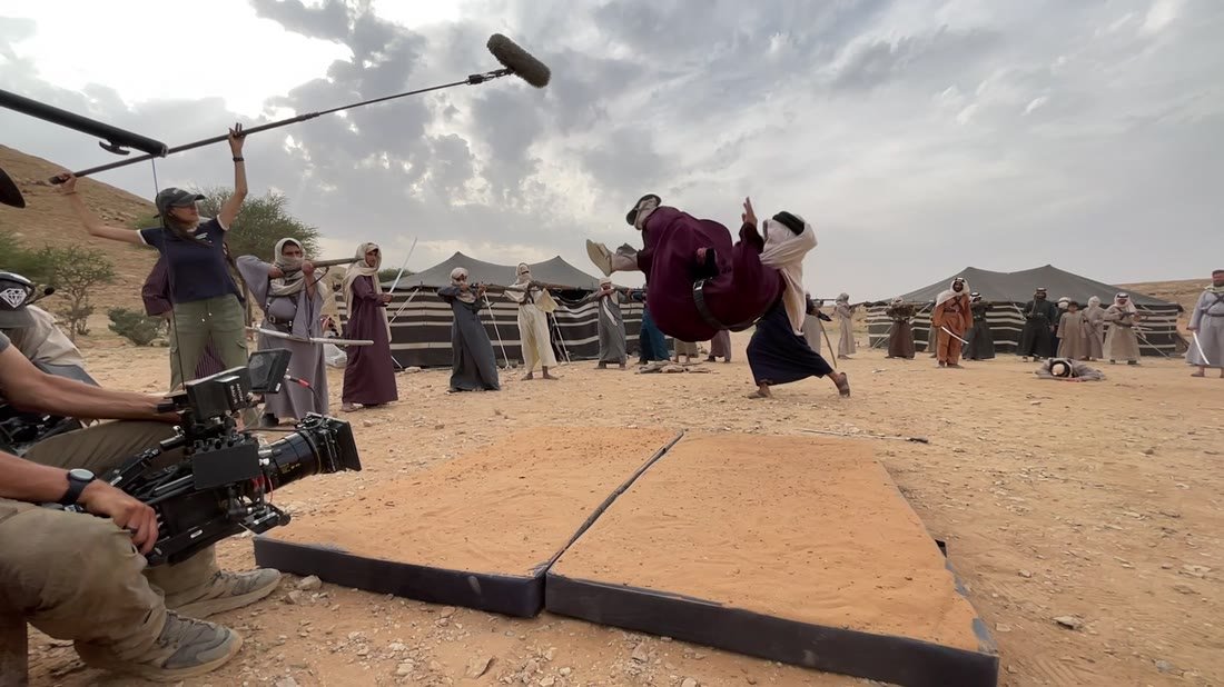 Behind the scenes on MBC's Sharar, desert south of Riyadh: a stunt performer mid-fall onto crash mats, with camera and boom operators nearby